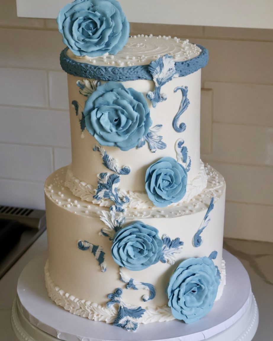 Two-tier white cake with blue sugar roses and scrollwork
