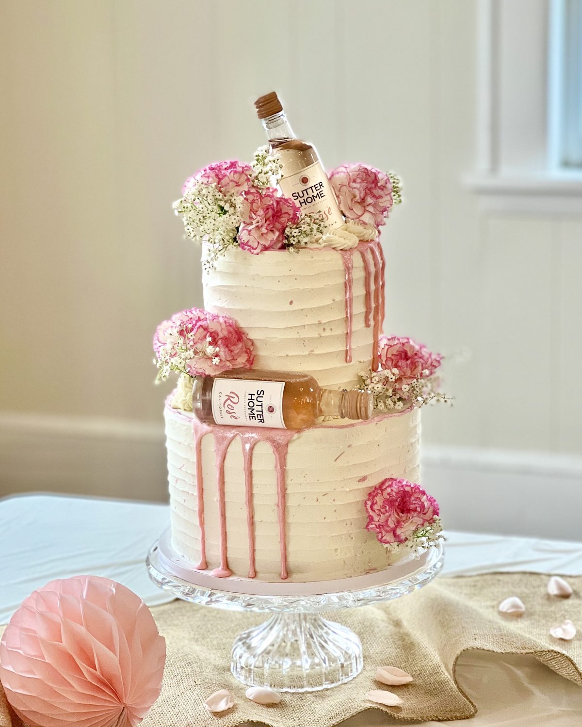 Pink drip shower cake topped with flowers and champagne