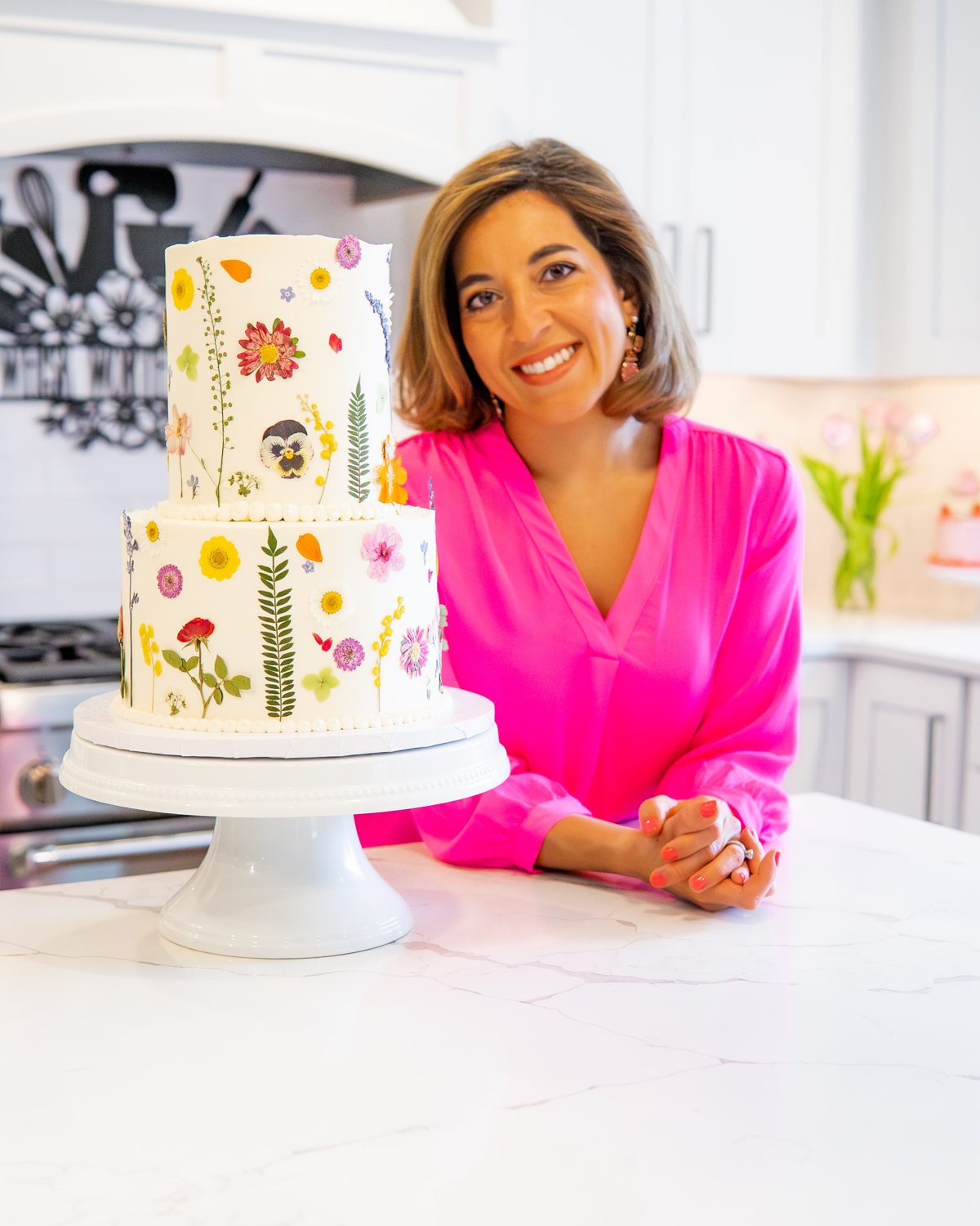 Cake artist Nika Spencer in her kitchen beside a wildflower cake