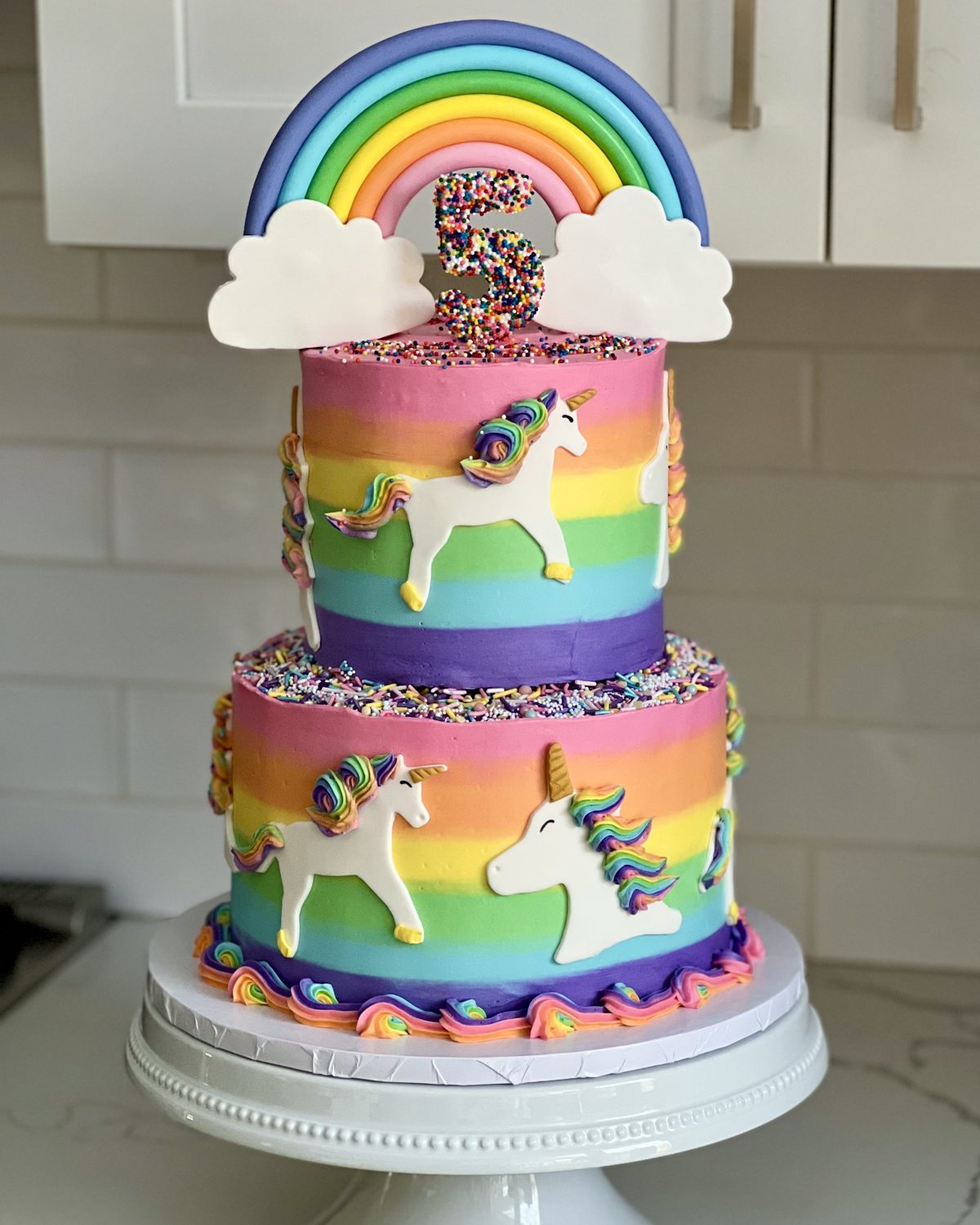 Two-tier rainbow birthday cake with unicorns and a fondant rainbow